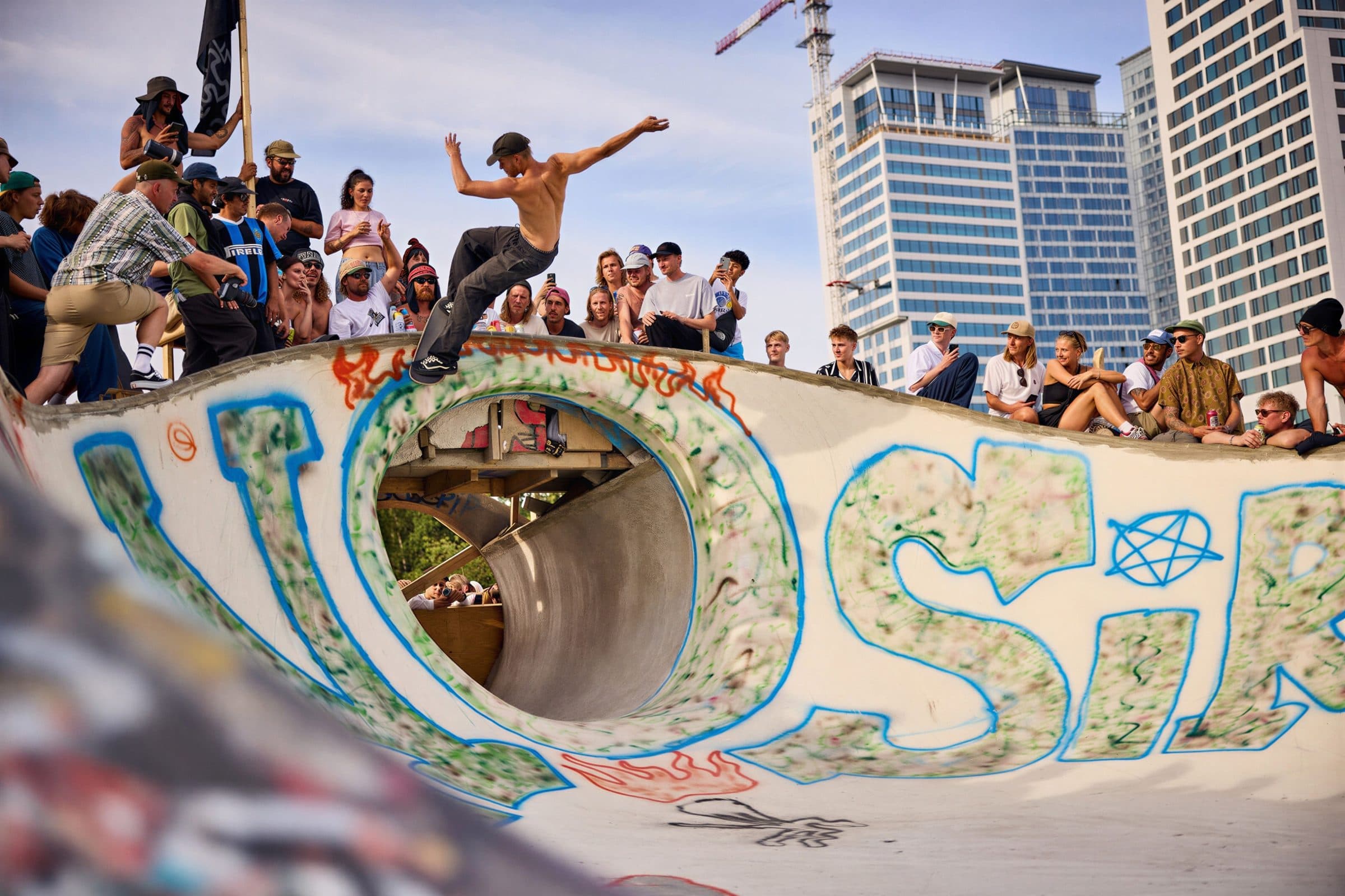 Skater grinding the lip of a graffiti-covered bowl while the crowd watches